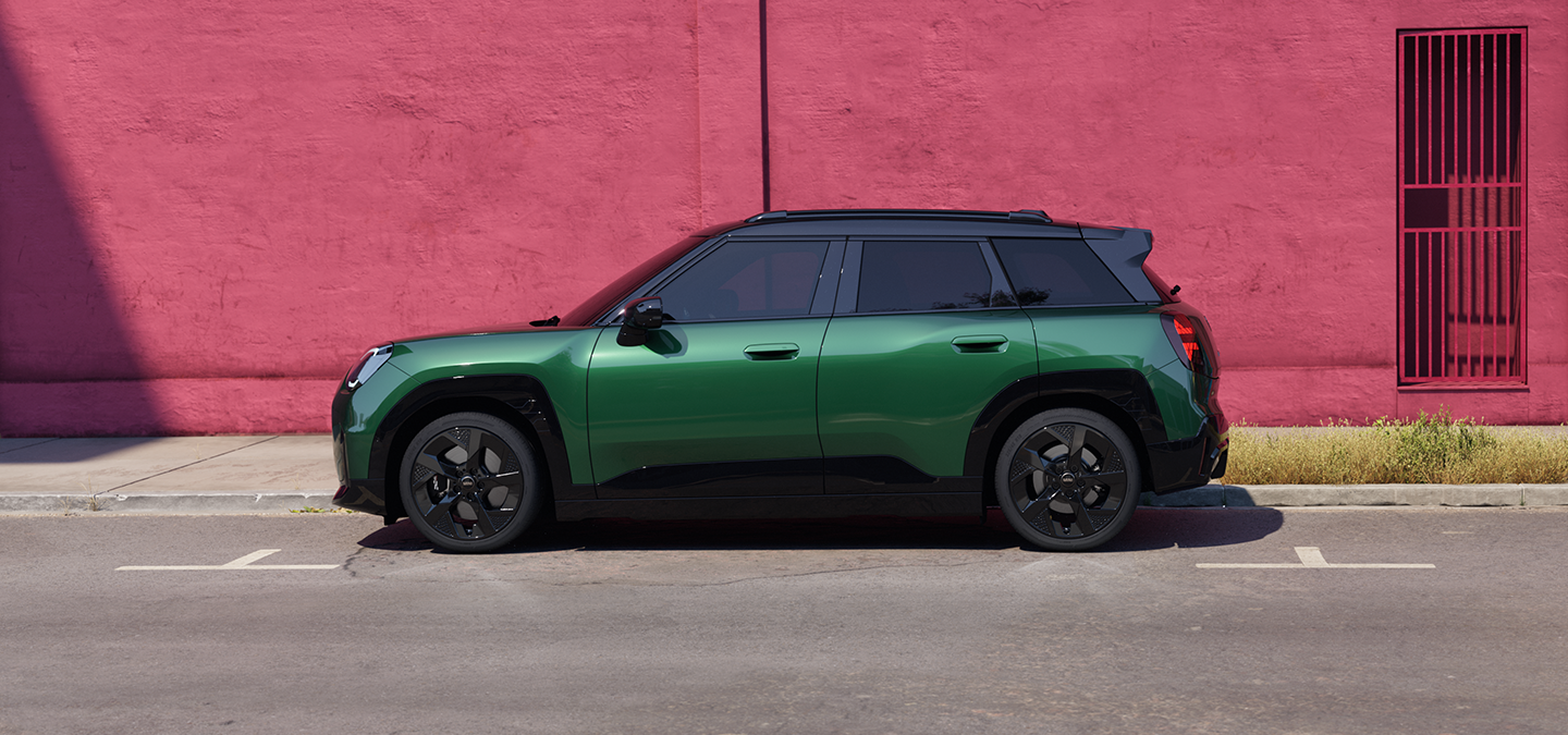 Vista lateral do MINI Aceman elétrico em Verde British Racing e tejadilho preto numa rua.