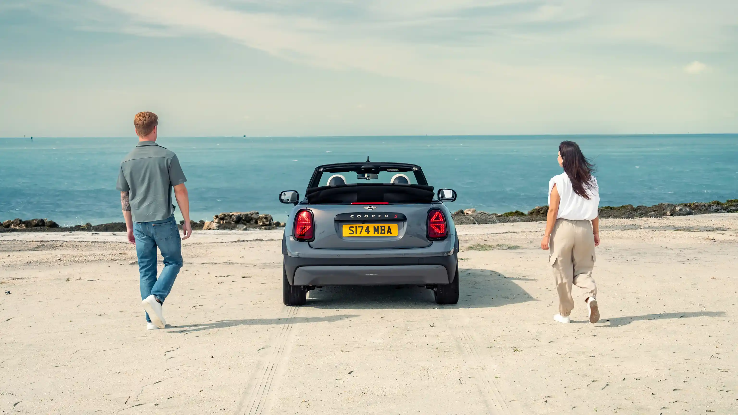 Vista traseira de um MINI Cooper Cabrio estacionado na praia, com duas pessoas