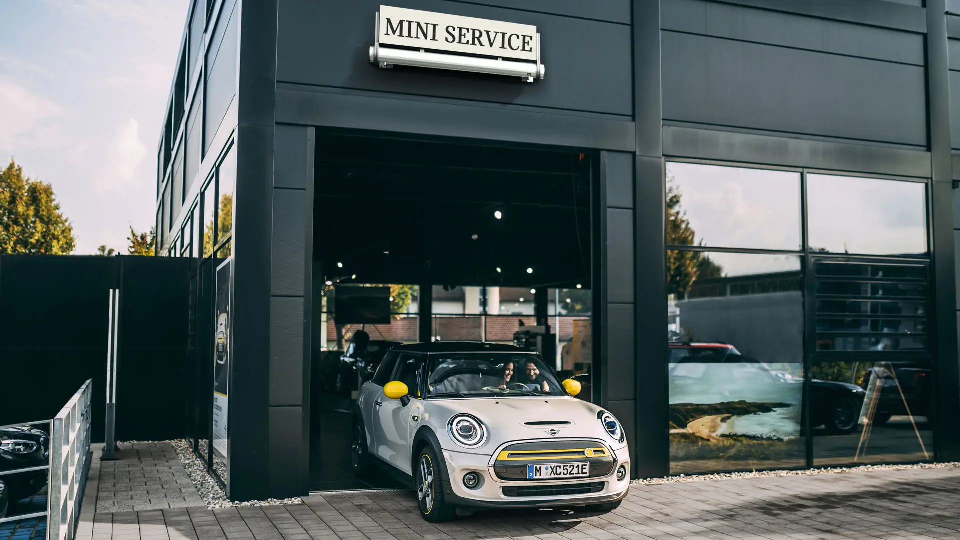Instalações do Ponto de Serviço Autorizado MINI com uma cliente a conduzir o seu novo MINI Electric até ao pátio