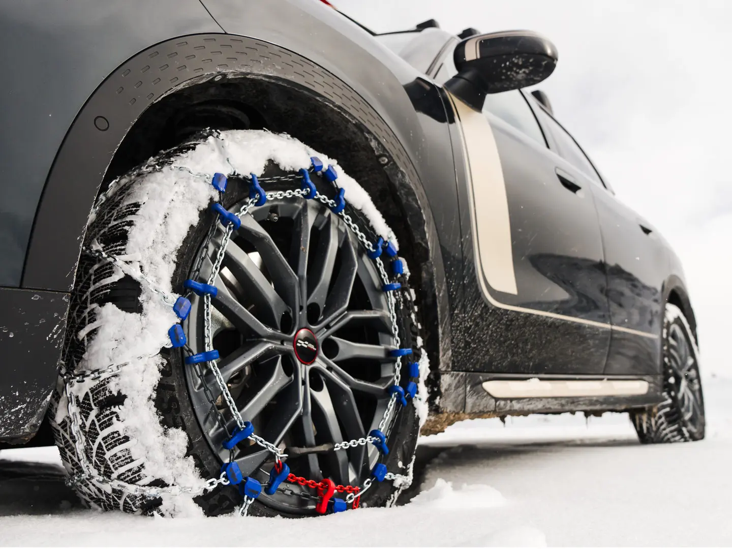 Grande plano de uma corrente de pneus instalada na roda de um MINI Countryman, para tração extra em condições de neve intensa. 