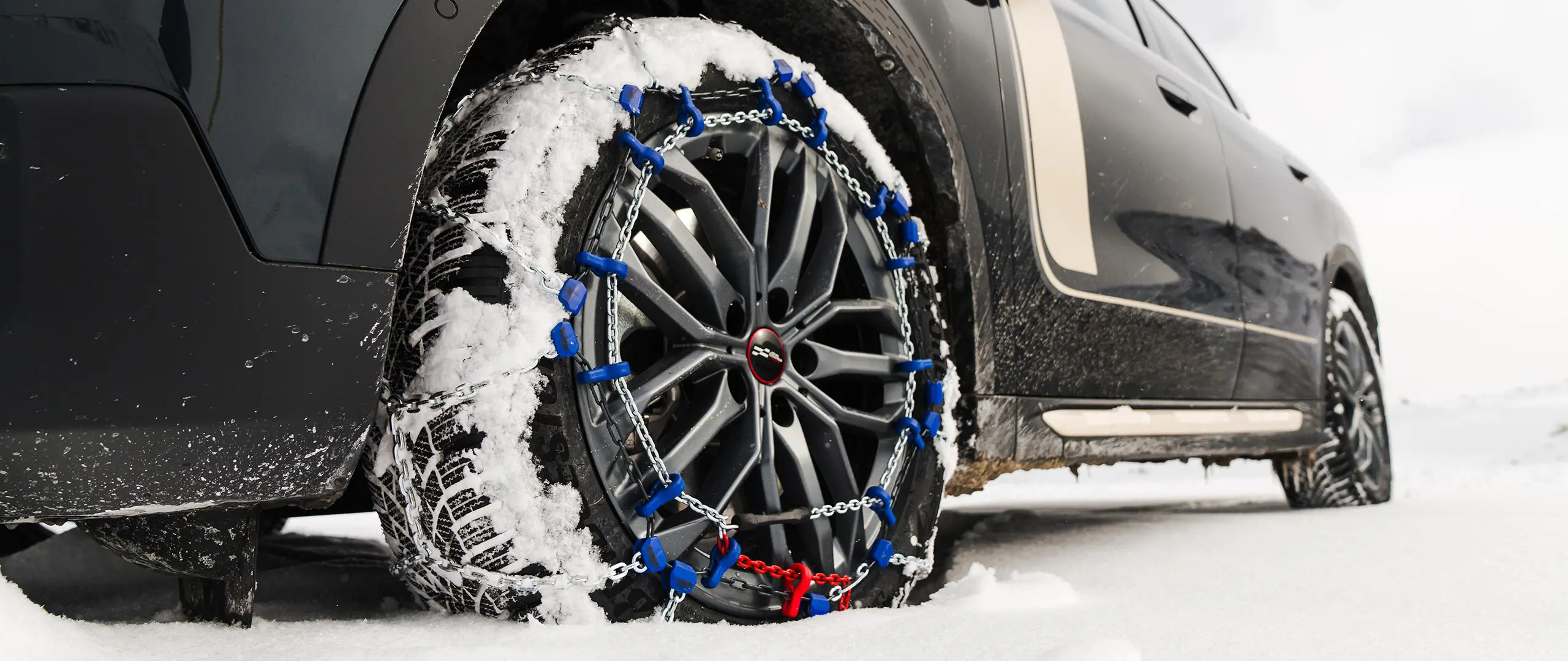 Grande plano de uma corrente de pneus instalada na roda de um MINI Countryman, para tração extra em condições de neve intensa. 