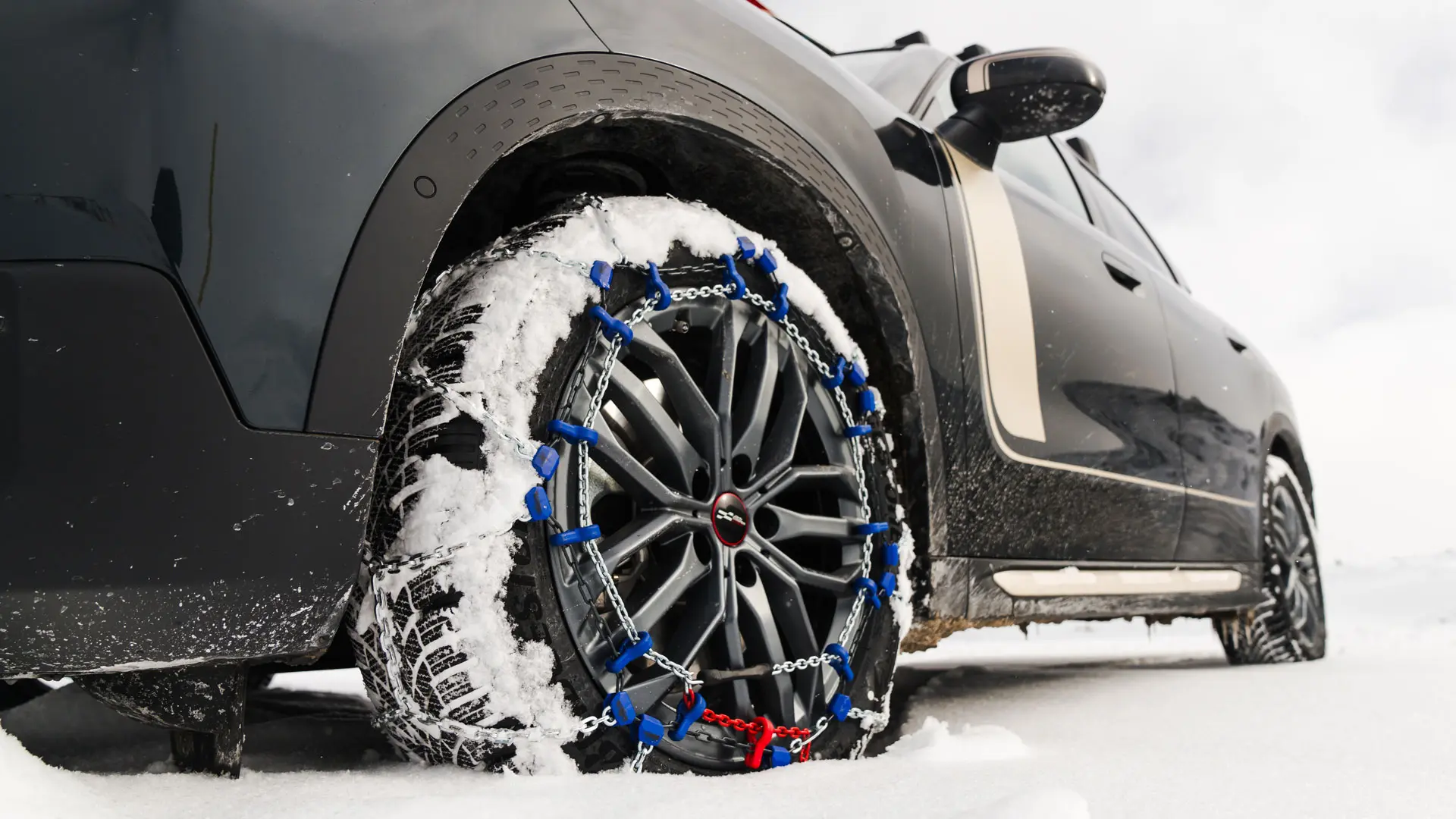 Grande plano de uma corrente de pneus instalada na roda de um MINI Countryman, para tração extra em condições de neve intensa. 