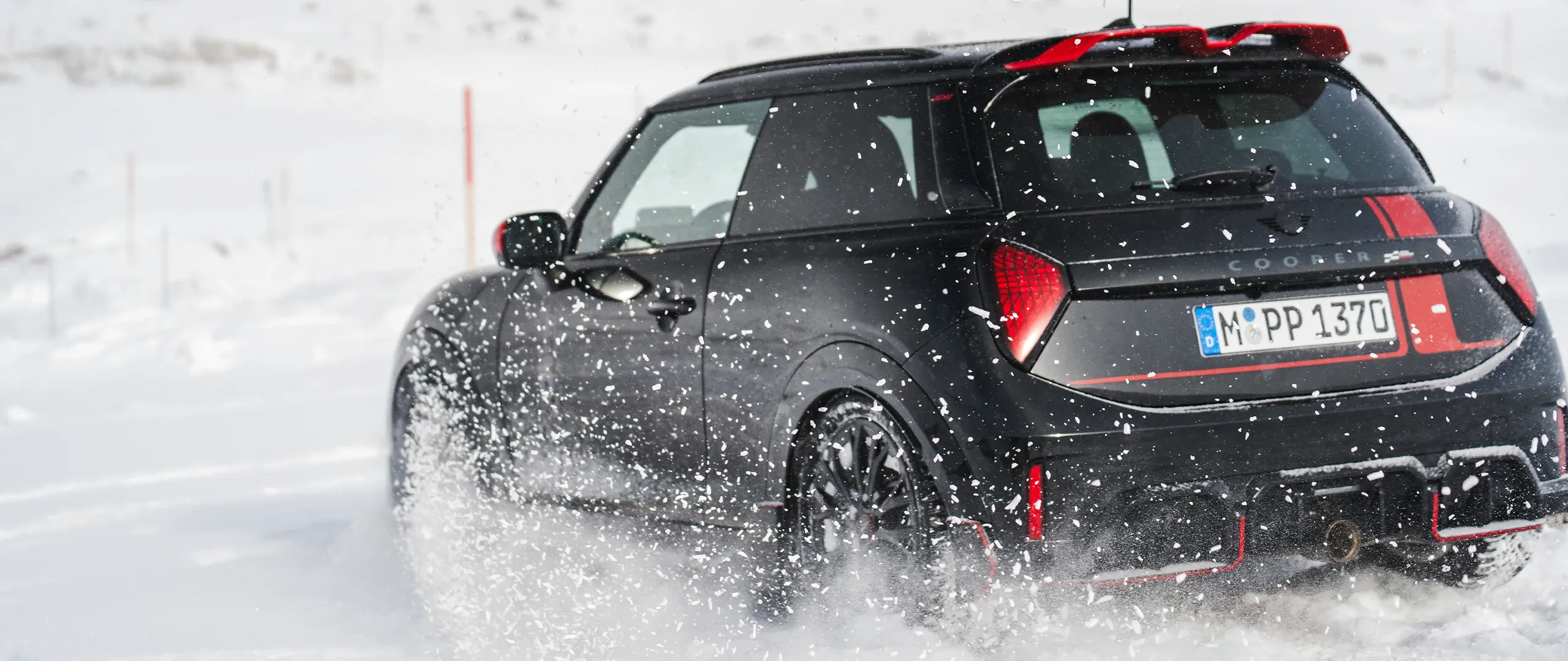 Vista traseira de um MINI Cooper JCW em regime de condução na neve.