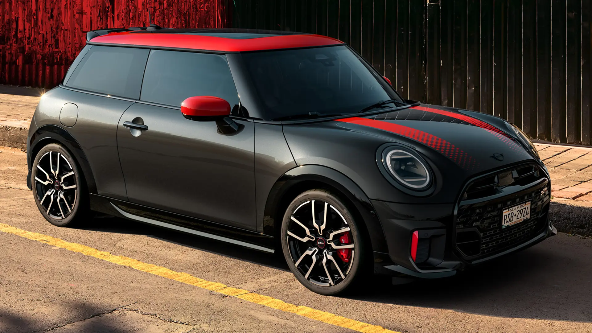 MINI John Cooper Works de 3 portas em Midnight Black com tejadilho e tampas dos espelhos retrovisores em Chili Red e faixas desportivas vermelhas, vista lateral, estacionado na rua.