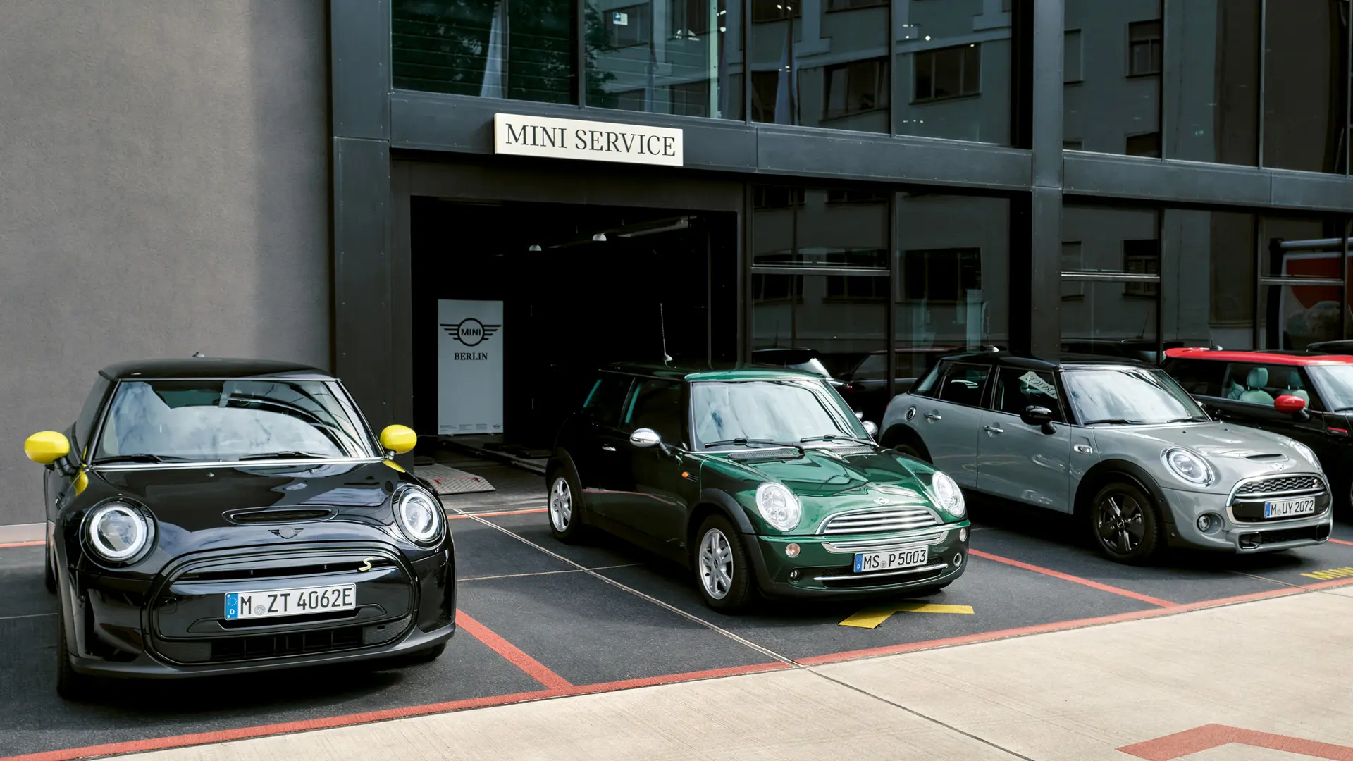 MINI Cooper S Elétrico em preto à porta de um concessionário MINI com um MINI Cooper de 3 portas verde, um MINI de 5 portas prateado, um MINI JCW preto, vista frontal. 