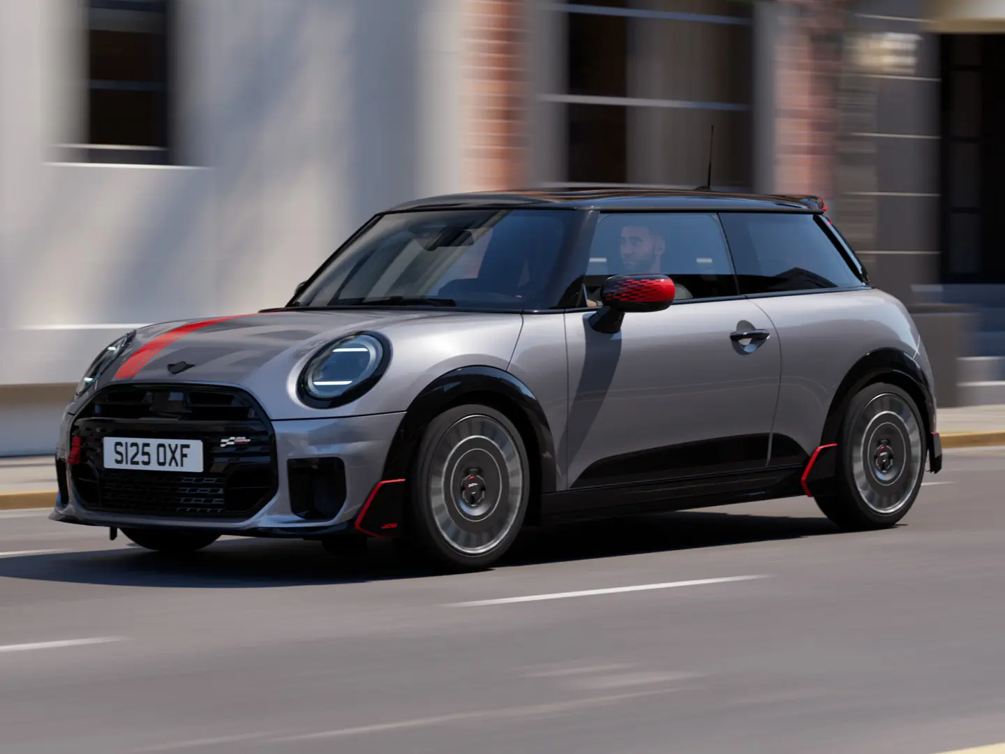 MINI Cooper de 3 portas em Melting Silver com tampa do retrovisor exterior John Cooper Works e decoração de capô em Chili Red, spoiler do tejadilho e winglet em Preto, circulando pelas ruas da cidade – vista frontal.