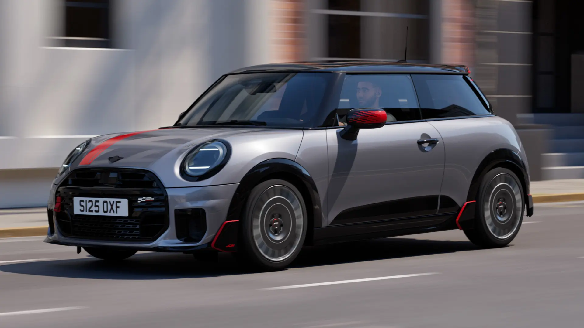MINI Cooper de 3 portas em Melting Silver com tampa do retrovisor exterior John Cooper Works e decoração de capô em Chili Red, spoiler do tejadilho e winglet em Preto, circulando pelas ruas da cidade – vista frontal.