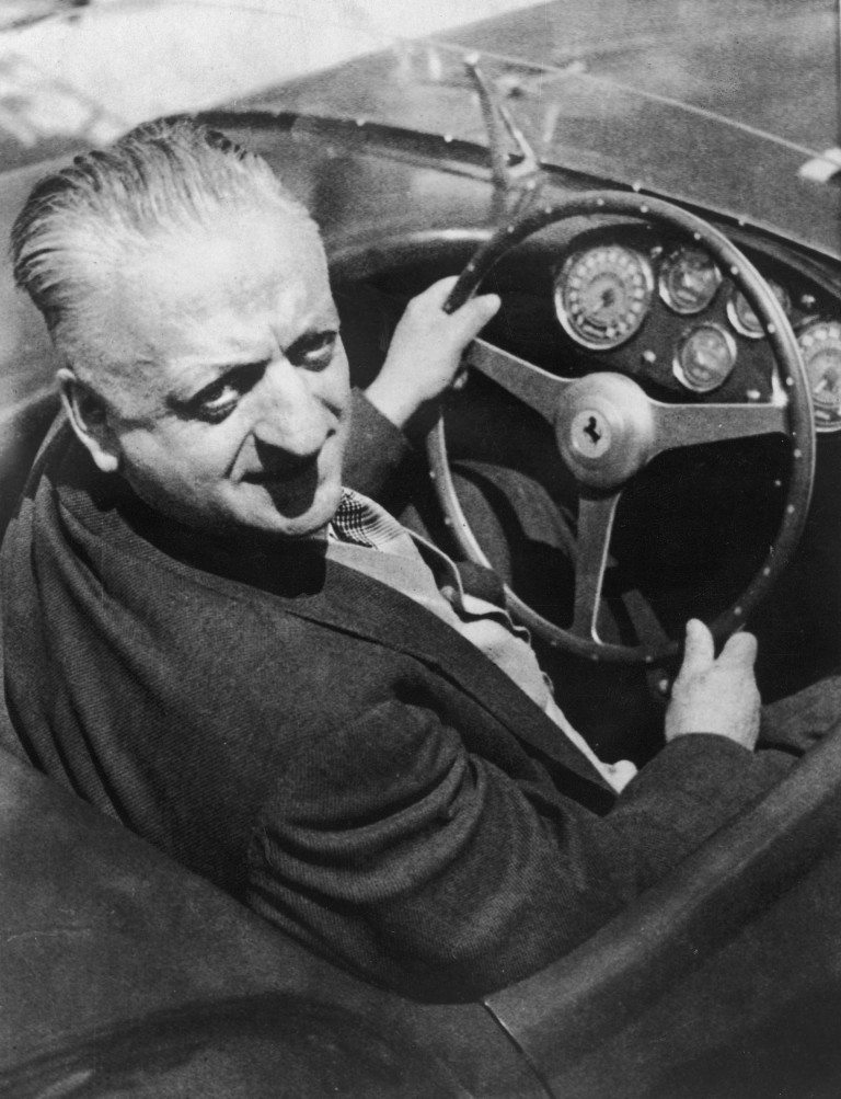 Fotografia a preto e branco de Enzo Ferrari sentado num Ferrari.