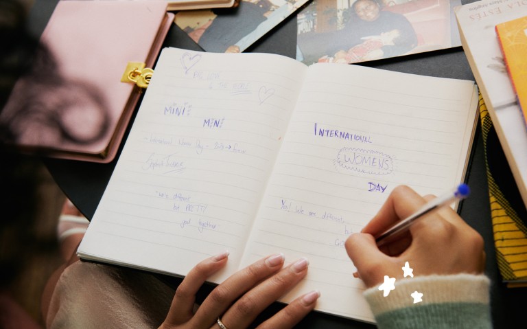 Sophia Thakur a escrever num caderno diferentes frases relacionadas com o Dia Internacional da Mulher MINI.