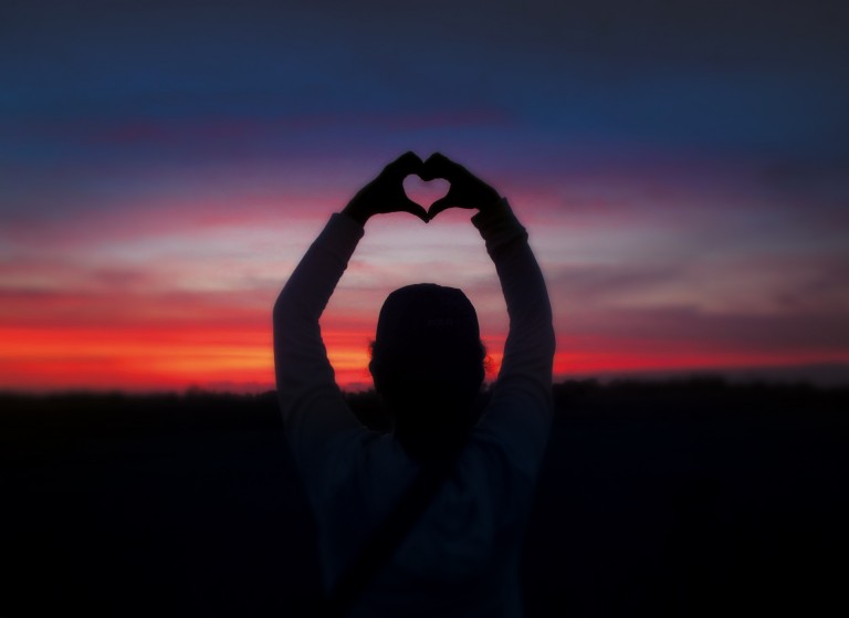 Foto do horizonte com pessoa de fundo fazendo um coração com as mãos.